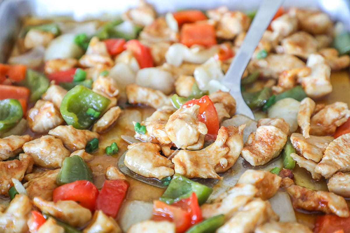 Pan of sheet pan orange chicken with spoon lifting off the pan