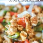 Pan of sheet pan orange chicken with spoon lifting off the pan