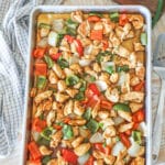 Pan filled with sheet pan orange chicken- with a kitchen towel in background