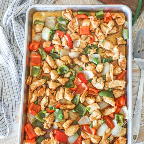 Pan filled with sheet pan orange chicken- with a kitchen towel in background