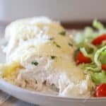 side view, closeup of a piece of cheesy garlic chicken on a plate with a side salad.