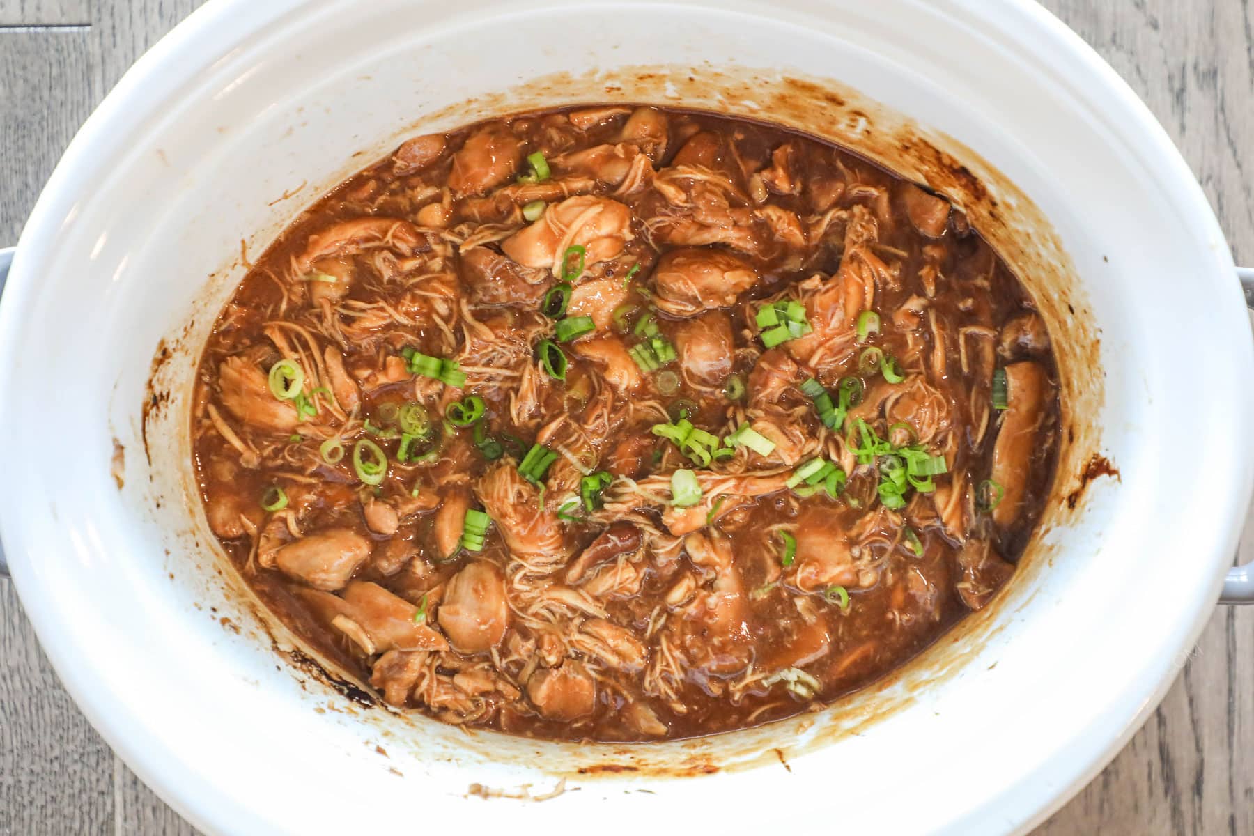 Finished slow cooker huli huli chicken in the crockpot garnished with green onions.