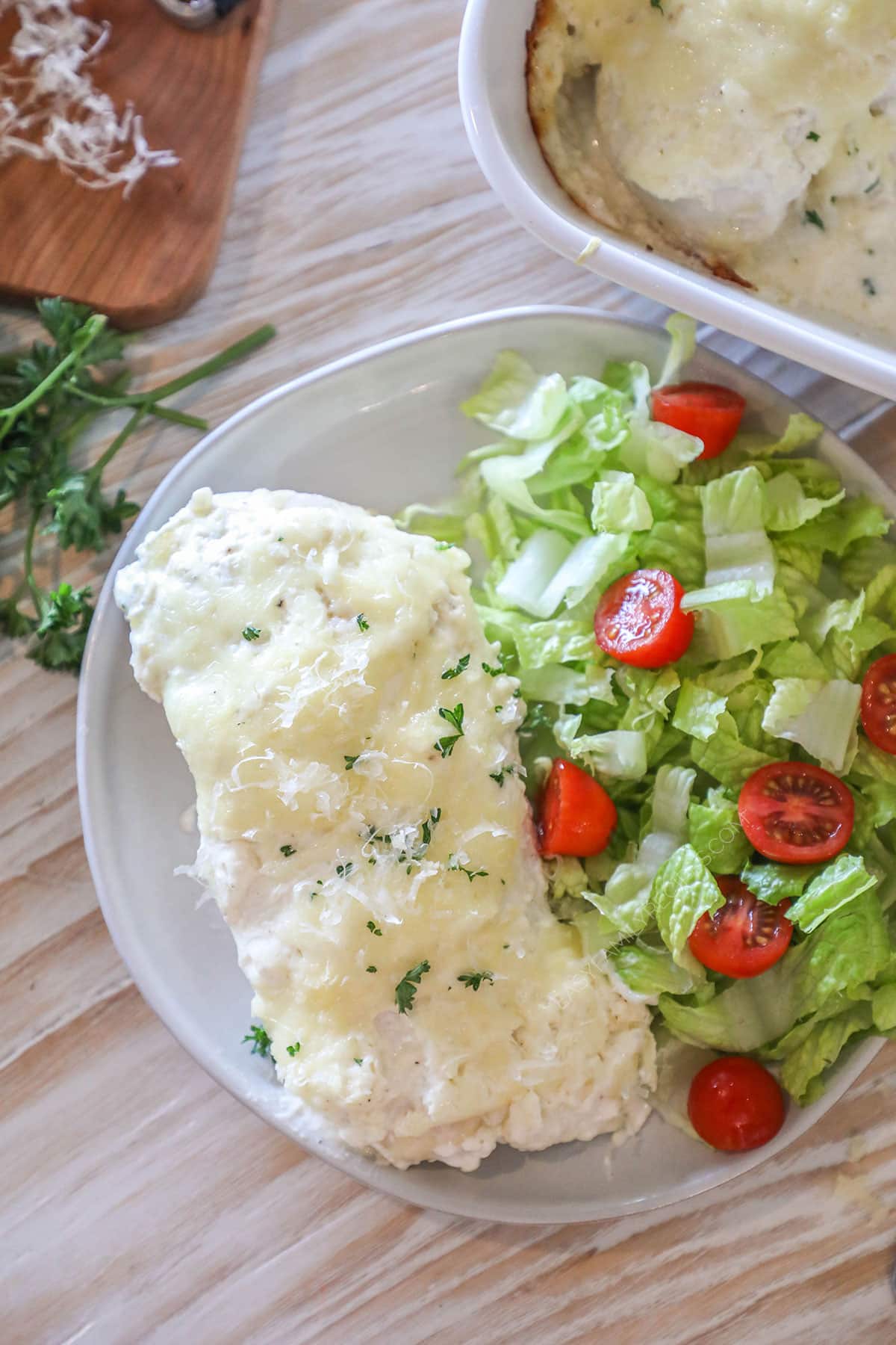 a slice of cheesy chicken on a plate with a side salad from above.