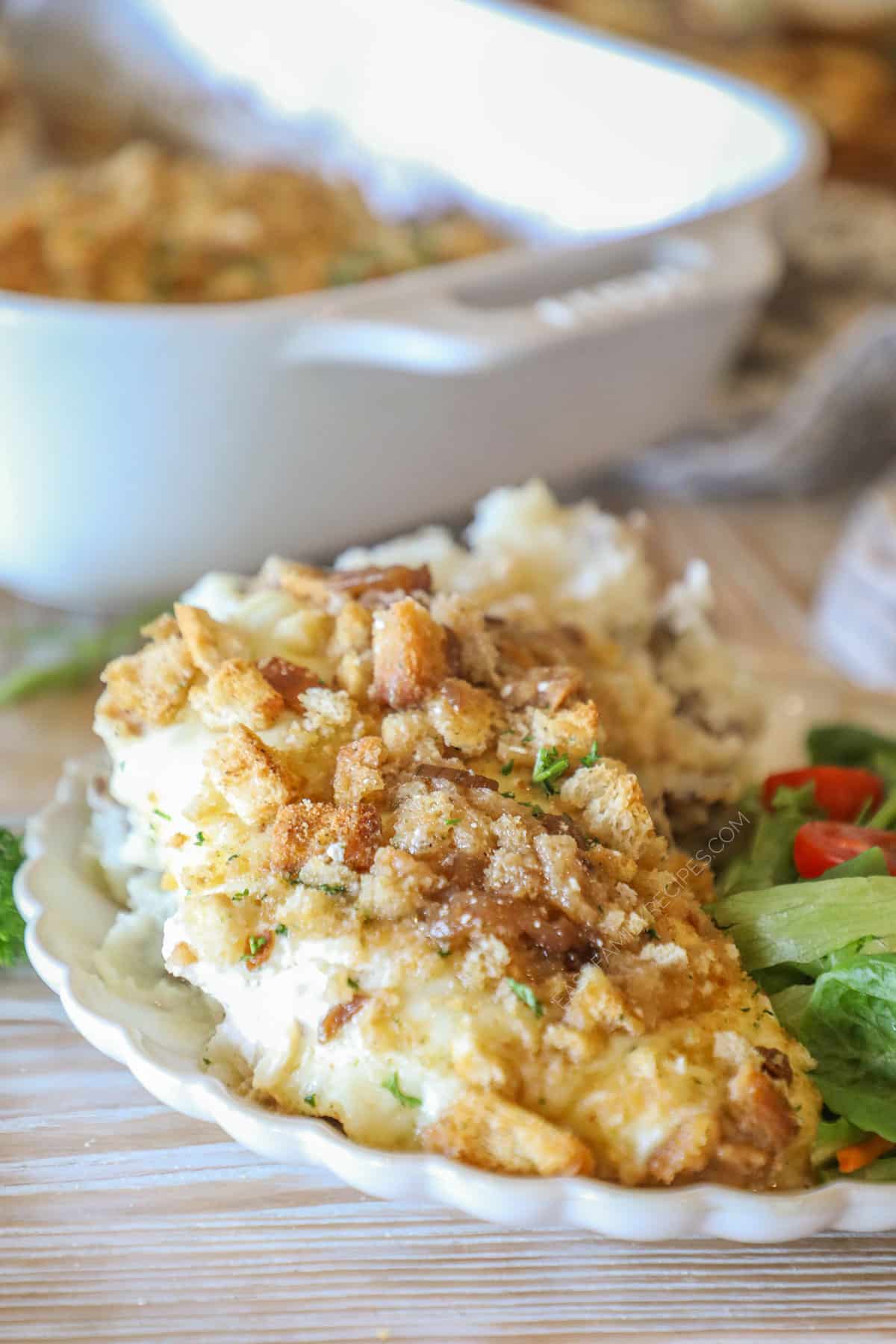 Individual serving of french onion chicken bake on white dish with side salad- on a wooden background with full pan in background