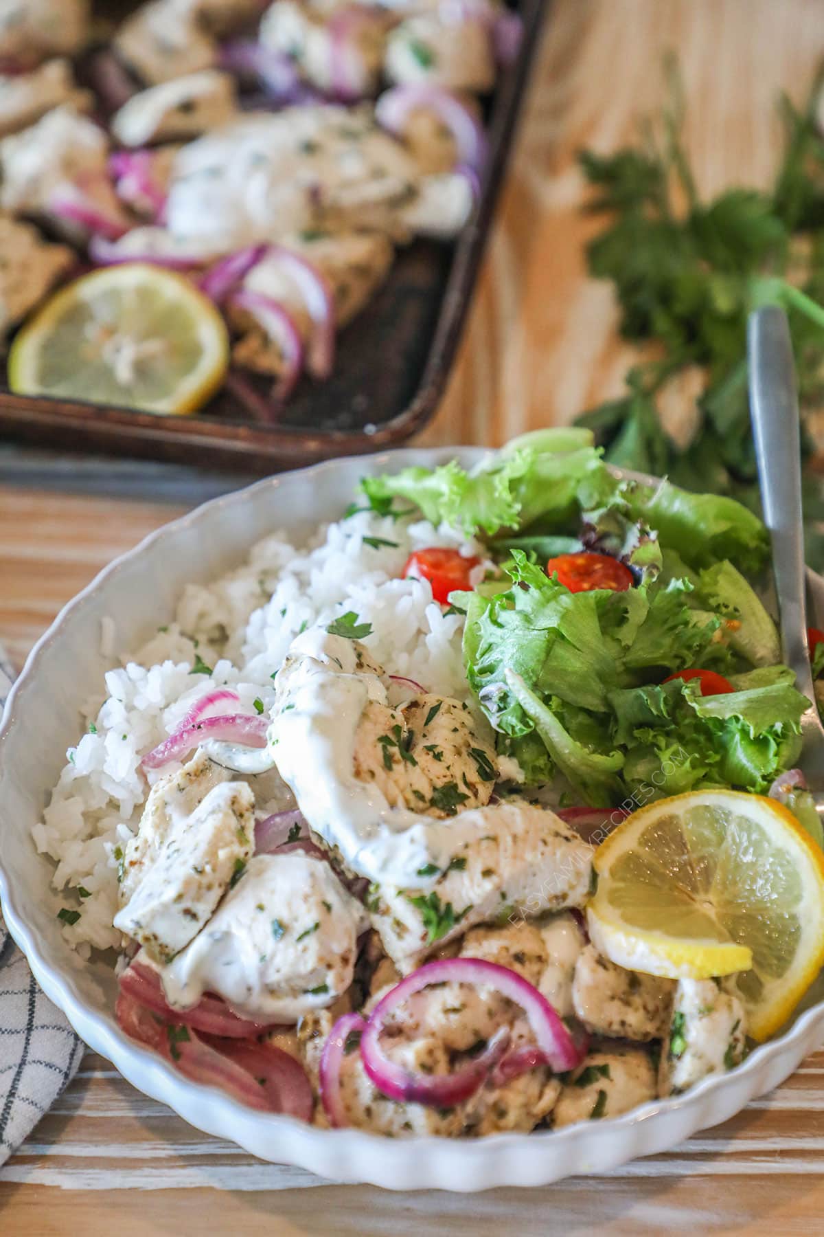 Sheet pan Mediterranean chicken served in a bowl with rice and lettuce.