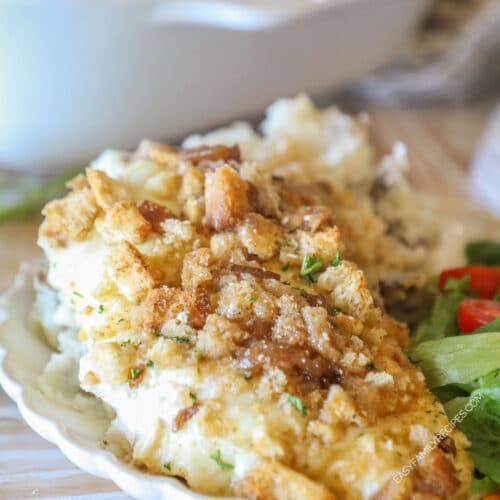 Individual serving of french onion chicken bake on white dish with side salad- on a wooden background with white pan in background