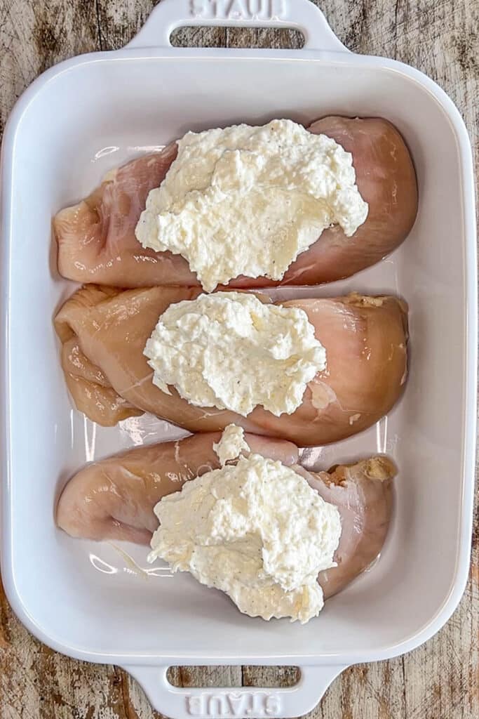 cream cheese sauce piled on three slices of chicken breast in a baking dish.