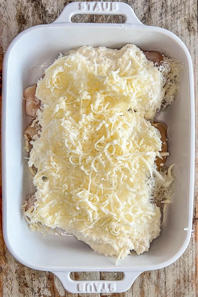 chicken breast in a baking dish topped with cream cheese mix and cheese.