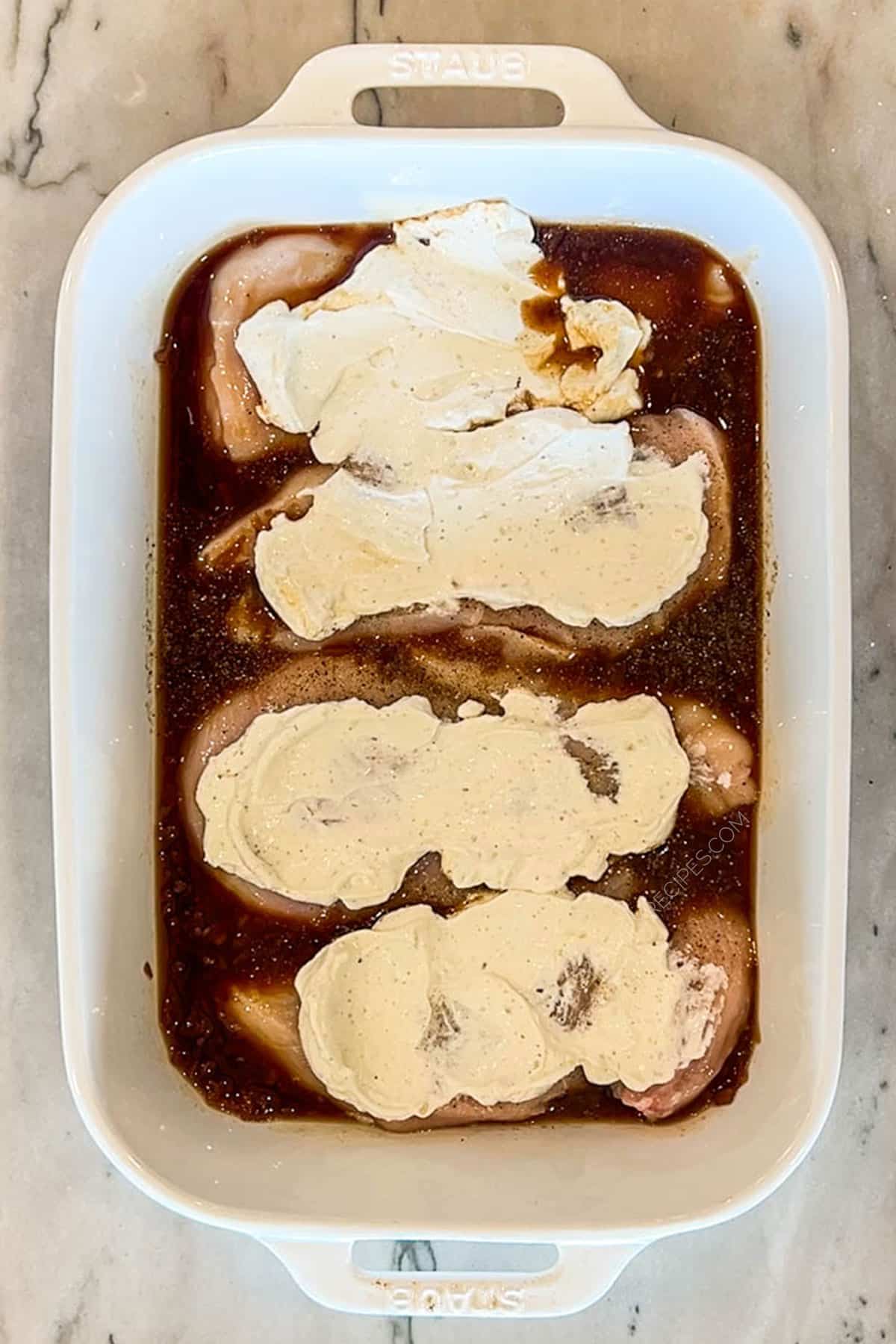 Step three of french onion chicken bake- chicken breasts topped with french onion dip, in white pan of french onion soup