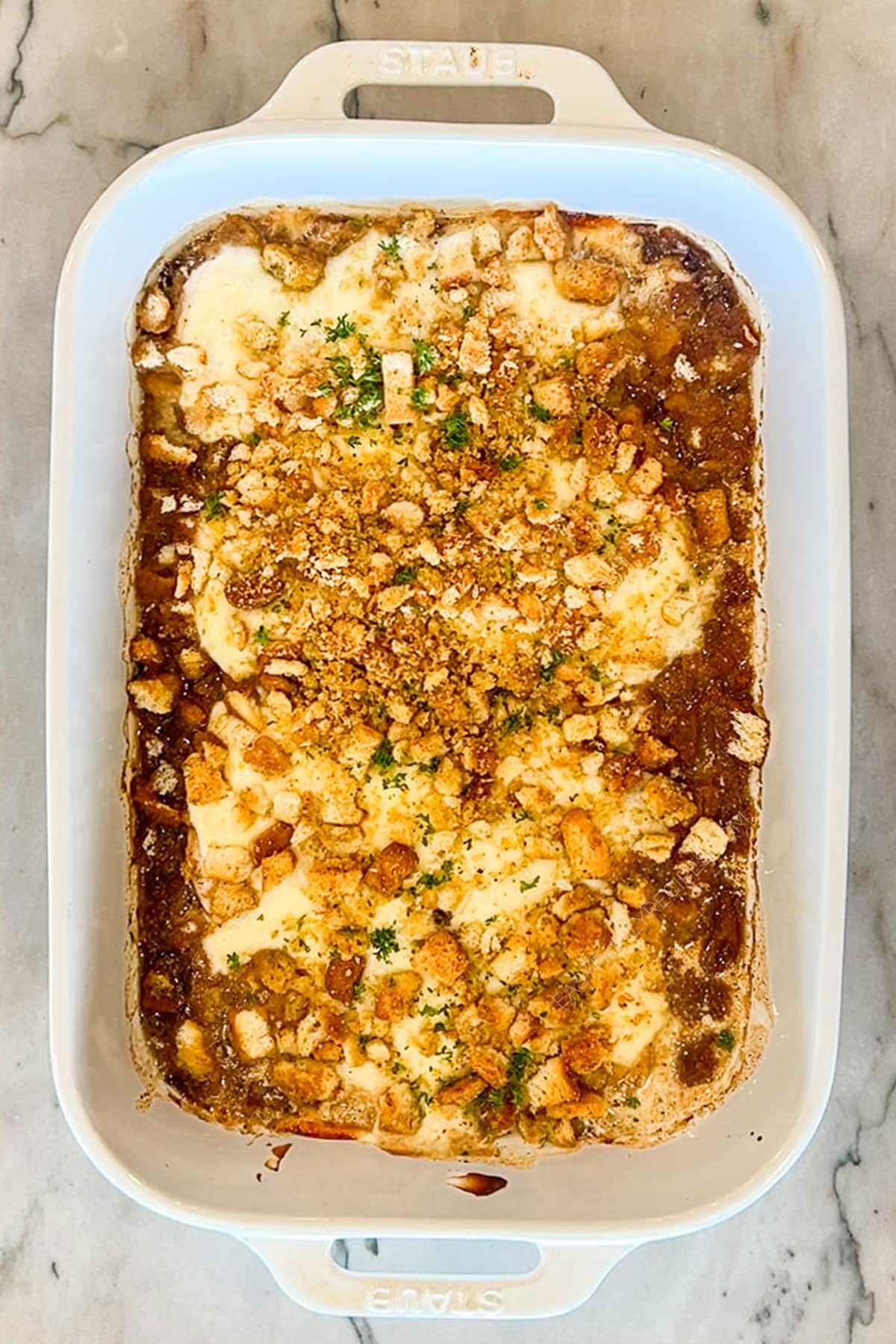 Step four of french onion chicken bake- chicken breasts in white pan- topped with crushed croutons