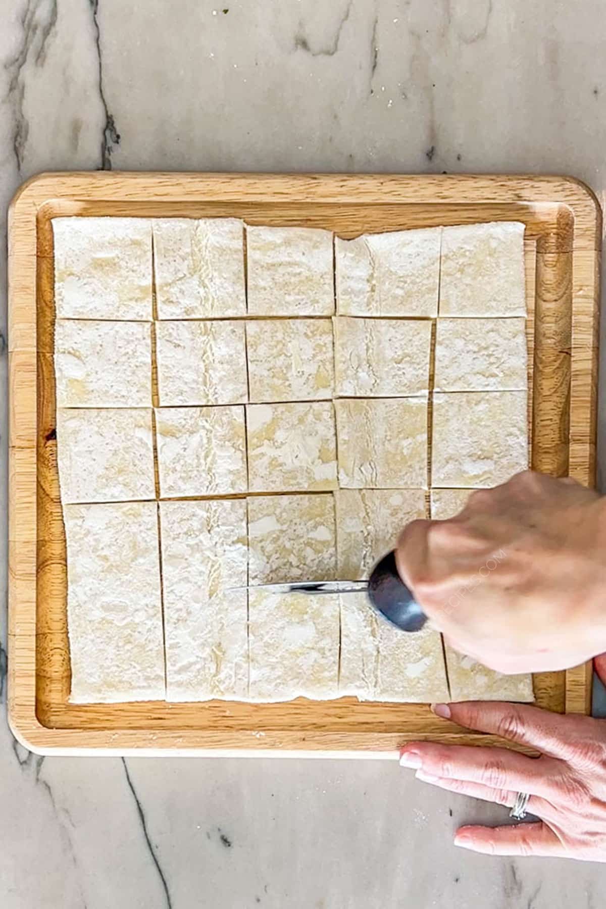 Step 1 for making Goat Cheese and Fig Jam Puff Pastry Bites. cutting pastry sheet on wooden board