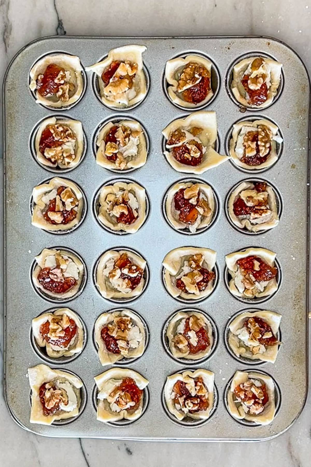 Step 2 for making Goat Cheese and Fig Jam Puff Pastry Bites. Pastry in tin muffin cups with goat cheese, fig jam and prosciutto