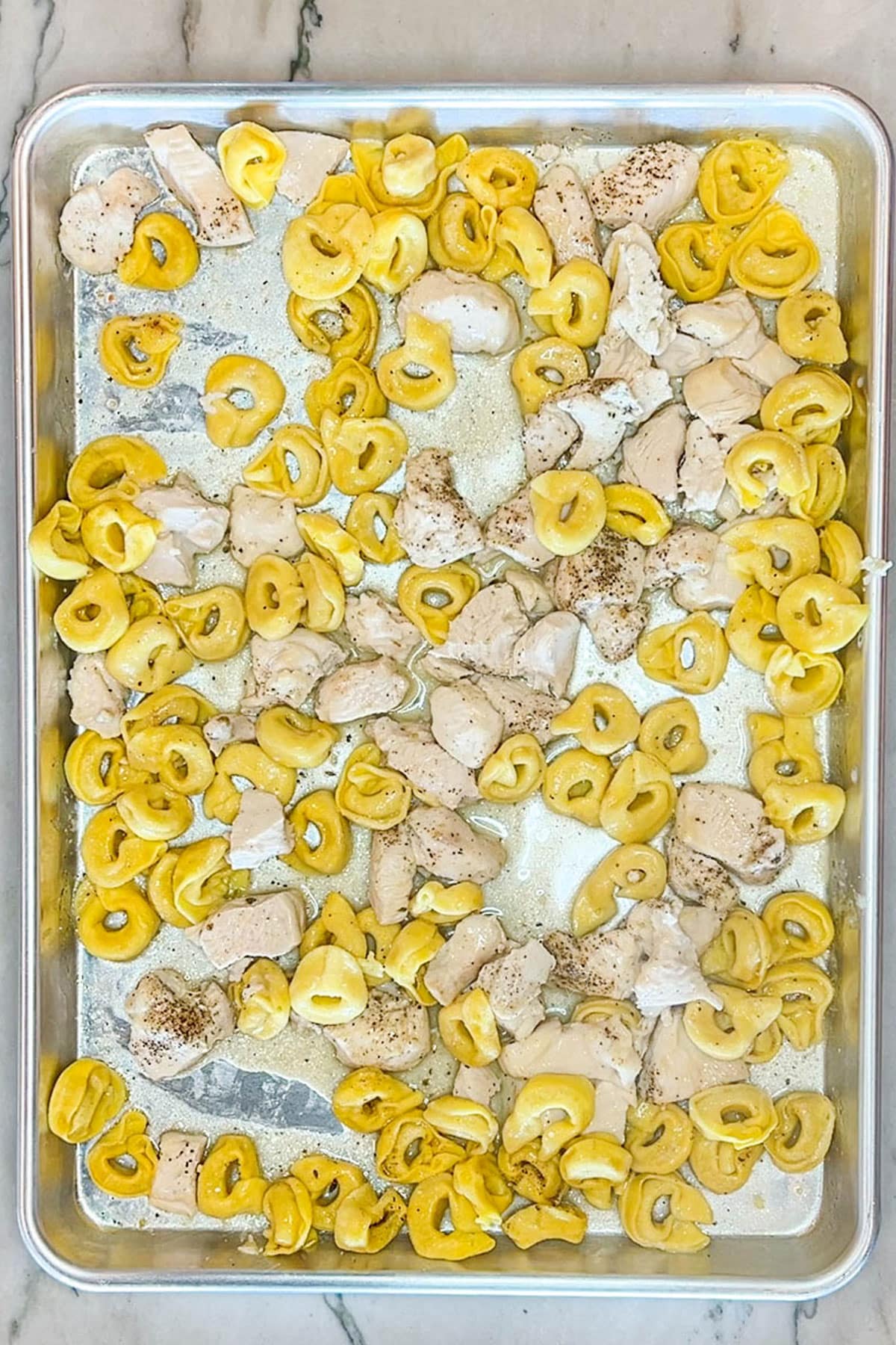 Baked tortellinis and diced chicken breast on a sheet pan.