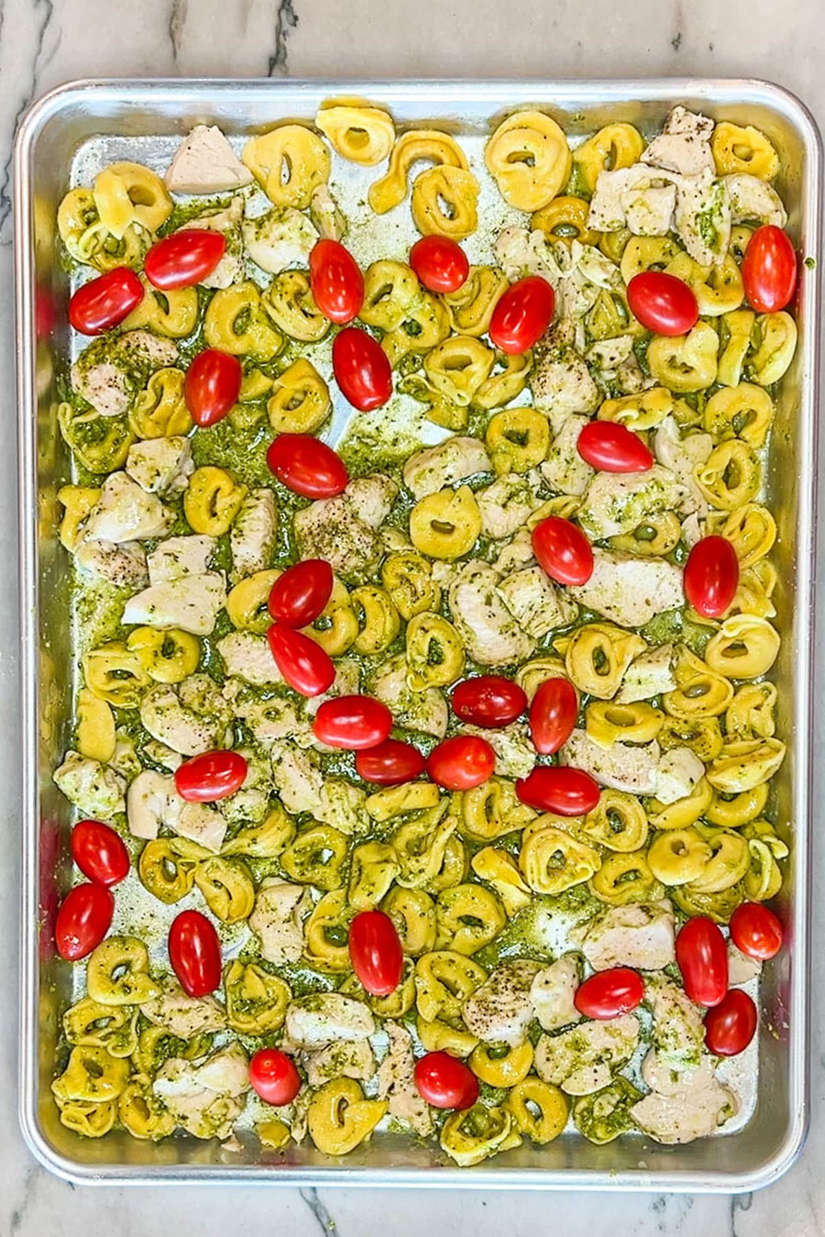 Tomatoes and pesto added to the chicken and tortellini on a sheet pan.