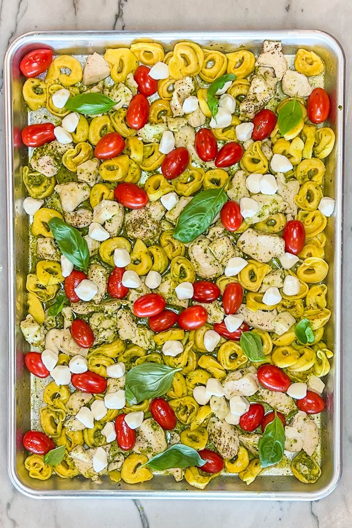 Fresh mozzarella and basil added to the caprese chicken and tortellini on a sheet pan.