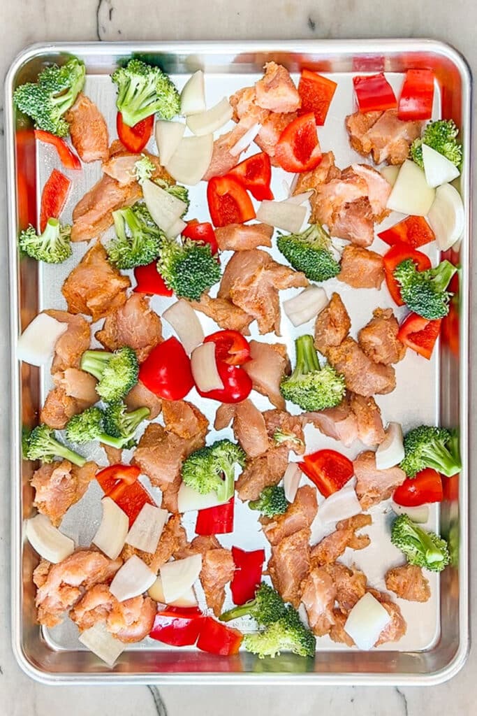 Seasoned chicken with veggies on a sheet pan before baking.