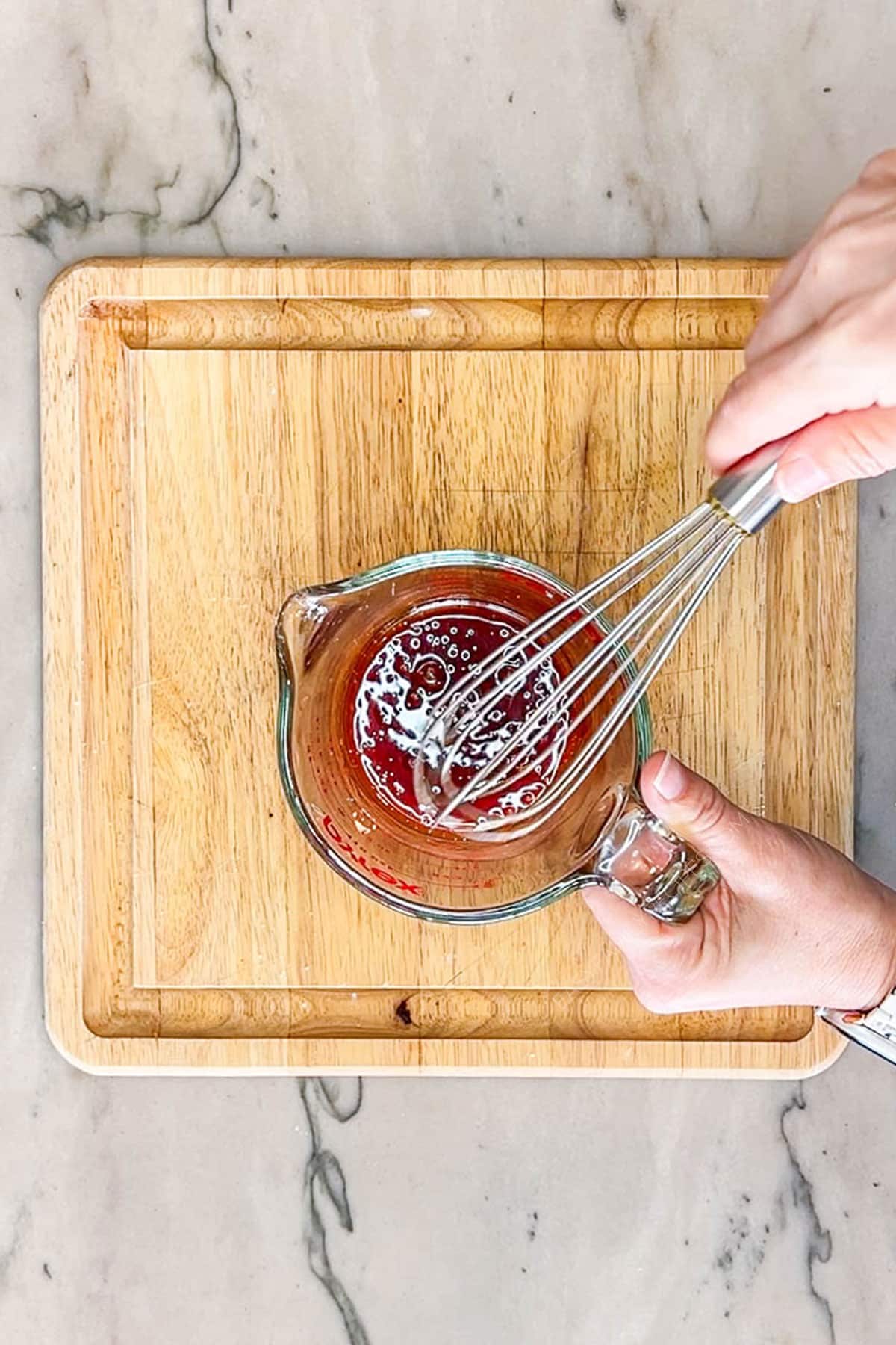 Two hands whisking together the hot honey mixture in a measuring cup.