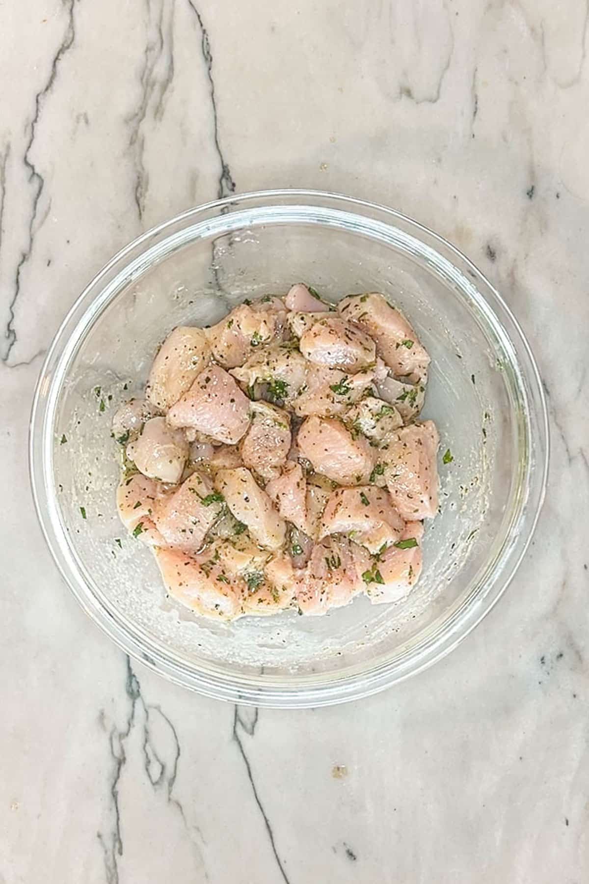 Diced chicken breast mixed together with a marinade in a bowl.