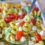 Metal spatula scooping up some sheet pan caprese chicken and tortellini.