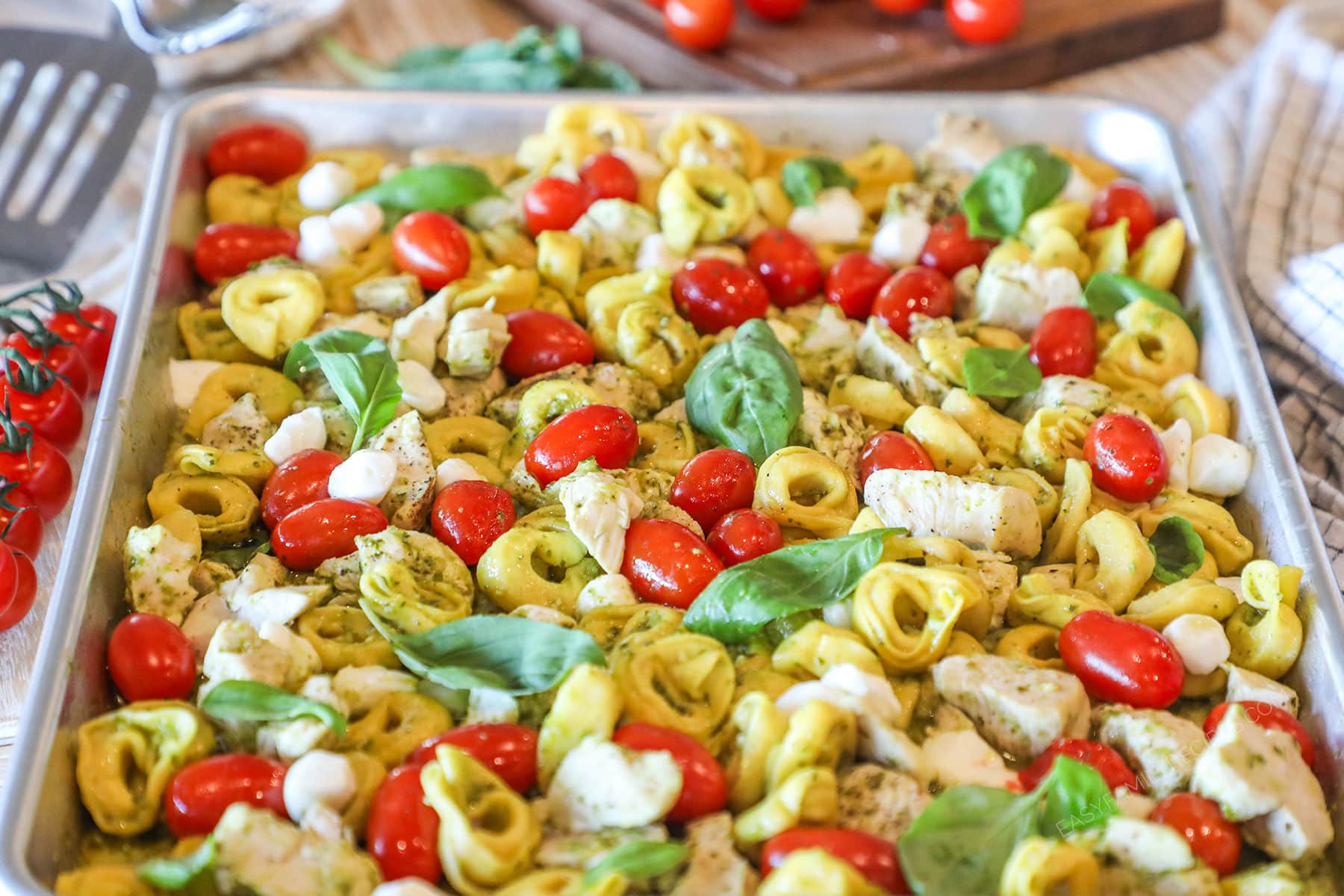 Side view of sheet pan caprese chicken and tortellini on a silver sheet pan.