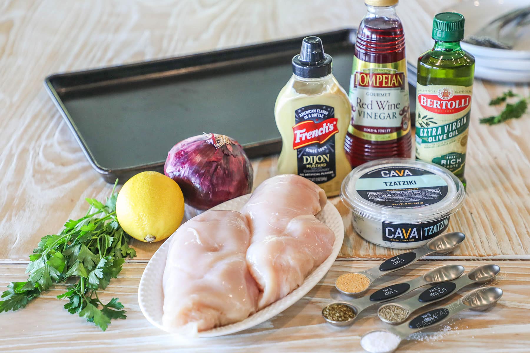 Ingredients needed to make sheet pan Mediterranean chicken on a wooden background.