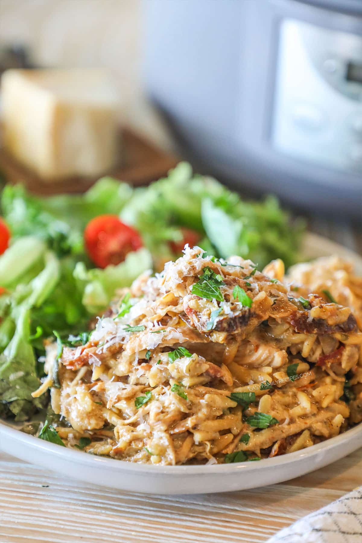 Crockpot Tuscan chicken and orzo served on a plate with salad.