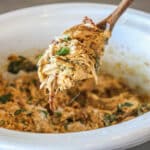 Wooden spoon with Tuscan chicken and orzo scooped from the crockpot.