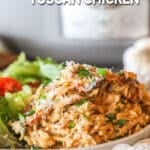 Crockpot Tuscan chicken served on a plate with a salad on the side.