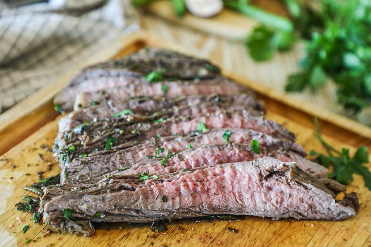 Flank steak cut on wooden board. Fresh herbs in background