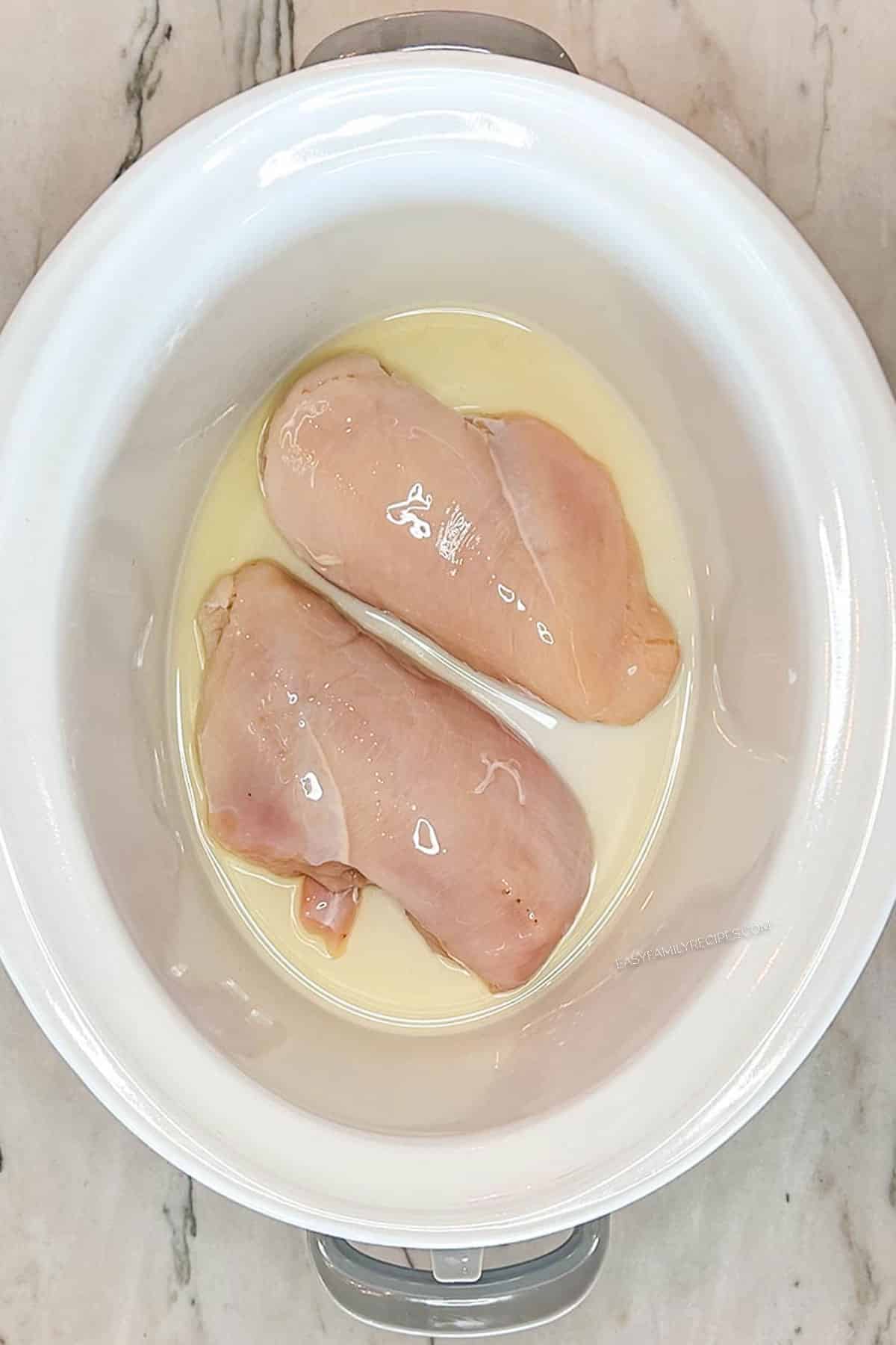 Step 1 for making Crockpot Million Dollar Chicken- add chicken breast and broth to the crockpot- in a white crock pot