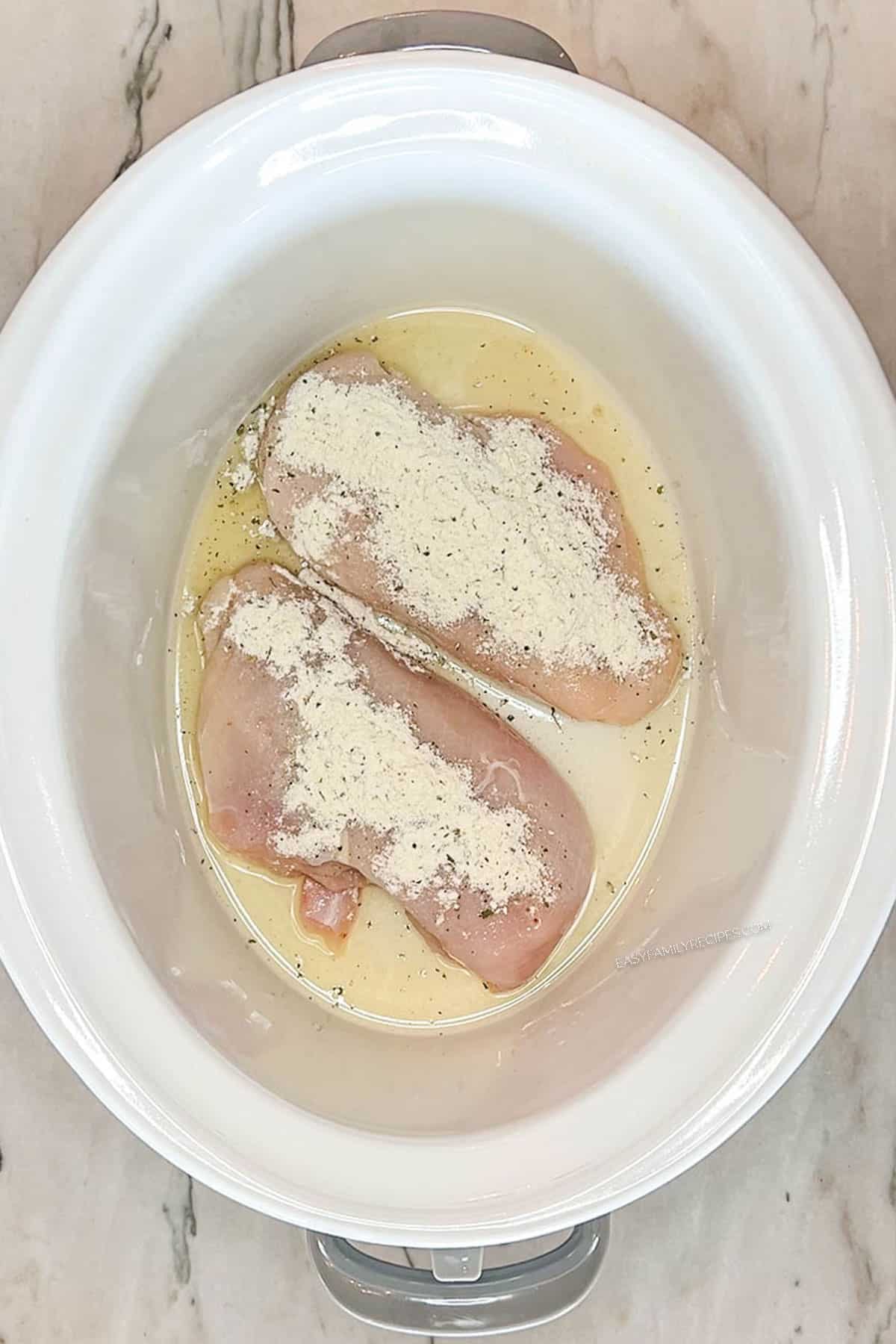 Step 2 for making Crockpot Million Dollar Chicken- add ranch seasoning to the chicken breasts. In a white crockpot