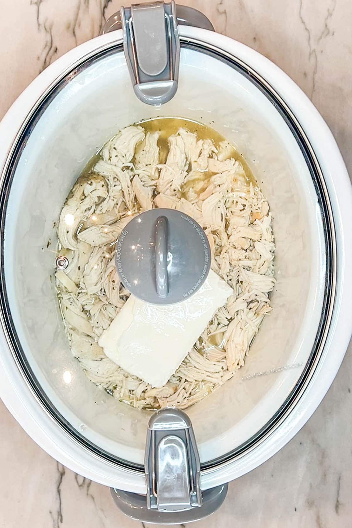 Step 4 for making Crockpot Million Dollar Chicken- Add cream cheese to soften. In a white crockpot with a lid on top
