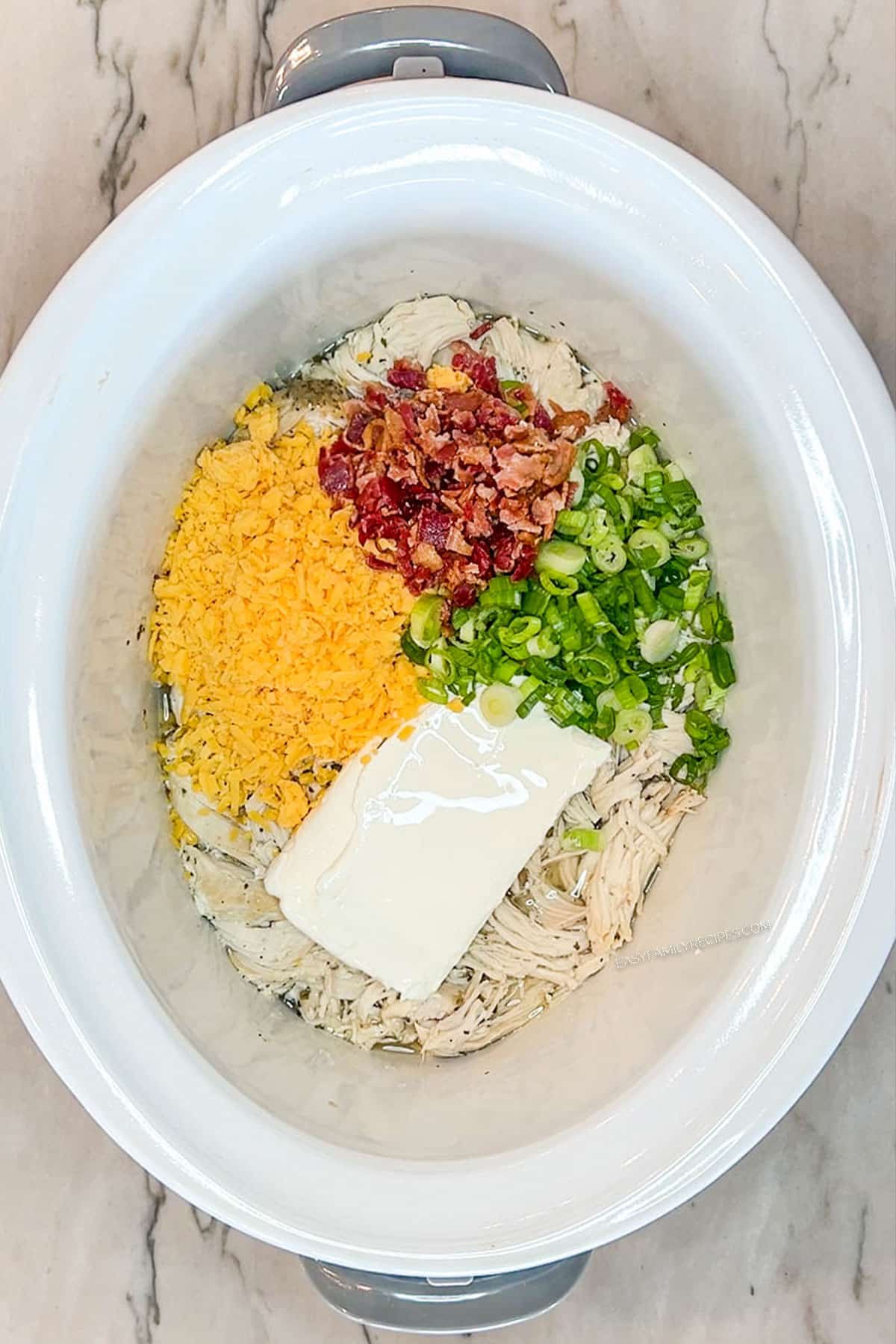 Step 5 for making Crockpot Million Dollar Chicken- Add shredded cheddar, bacon and green onions. In a white crockpot