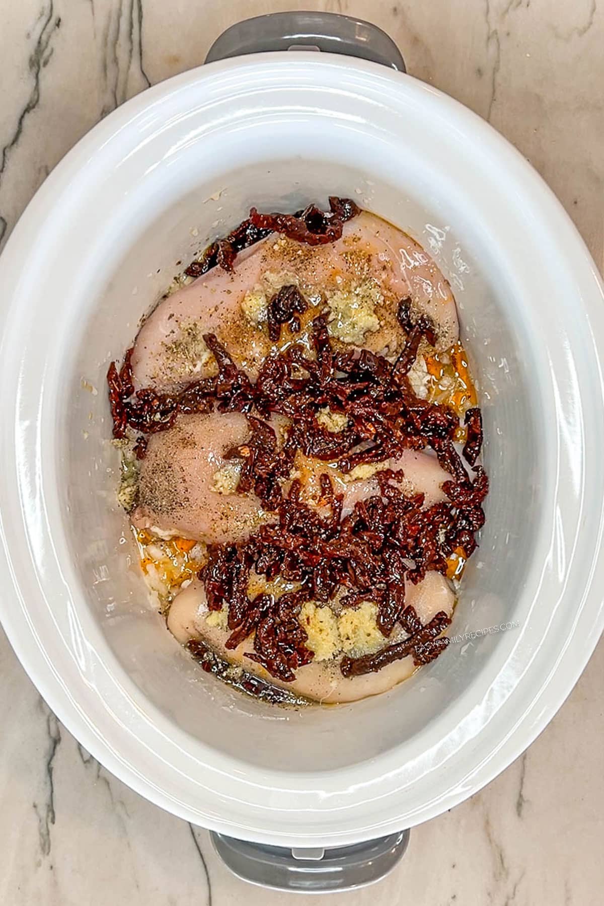 Chicken breast in the crockpot with onion, garlic, seasonings, and sun dried tomatoes.