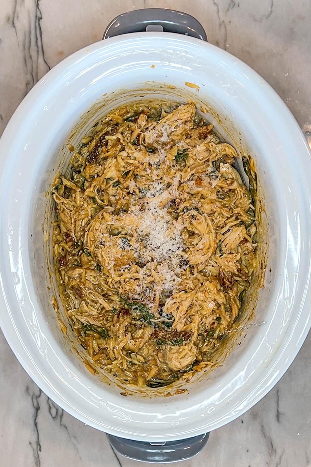 Tuscan chicken with orzo in the crockpot with parmesan on top.