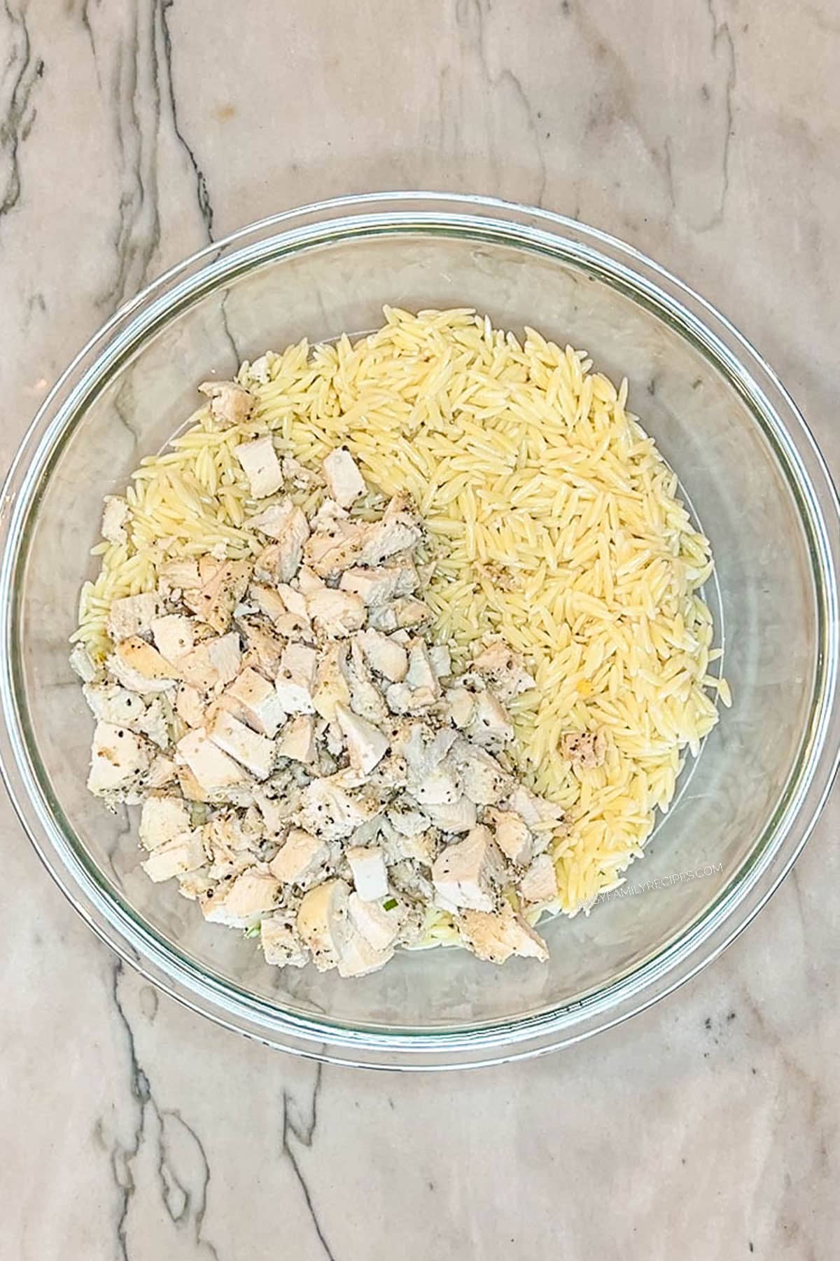 orzo and chopped chicken in glass bowl- on a marble background