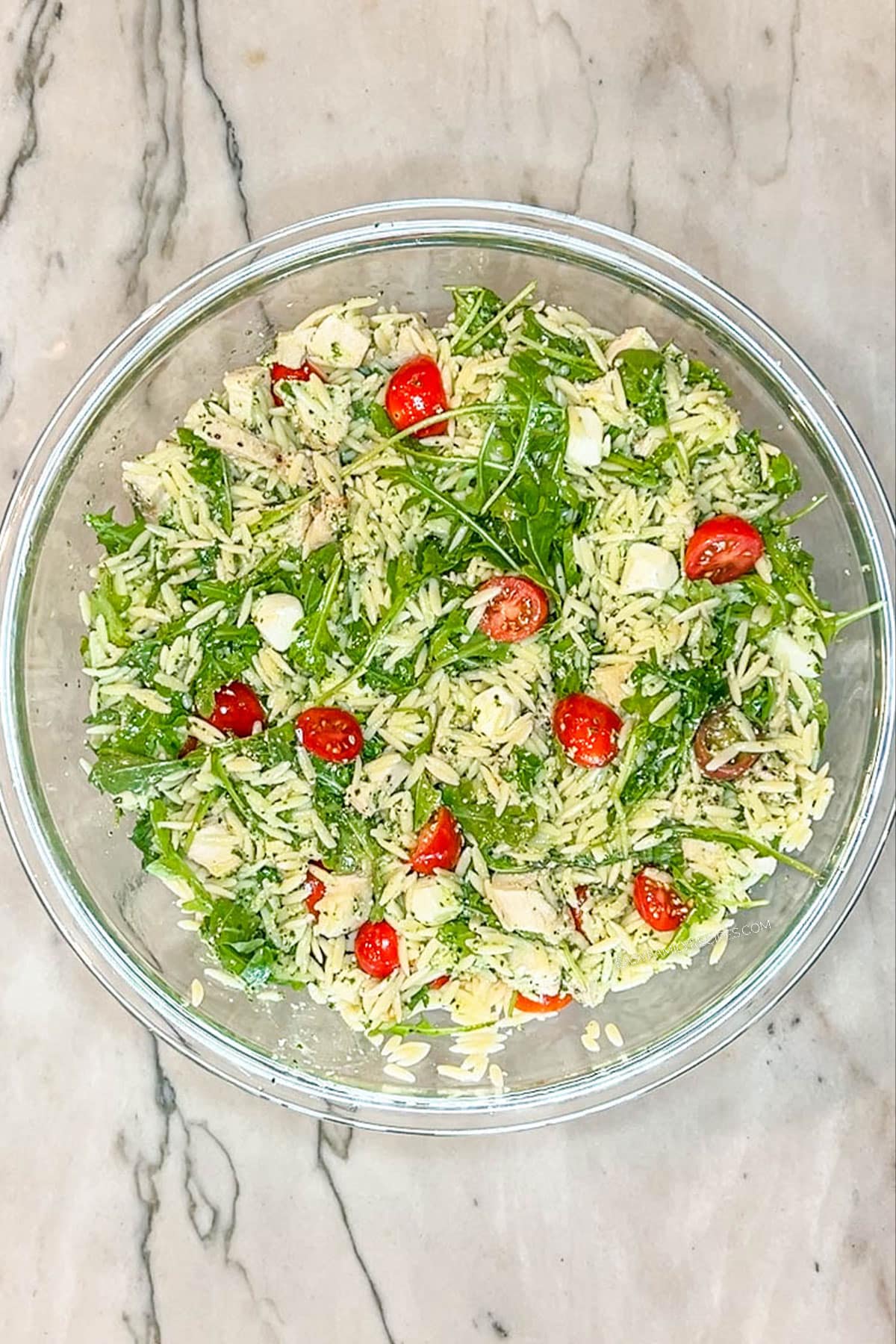 pesto chicken salad with orzo in glass bowl- on a marble background