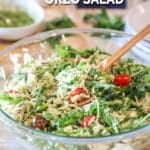 Pesto chicken salad with orzo in large, glass bowl with wooden spoon. On a wooden background