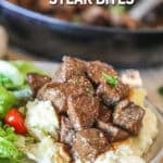balsamic steak bites over mashed potatoes with a side salad- on a white plate- pan of steak bites in the background