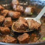 balsamic steak bites seared and cooked in cast iron skillet with metal spoon lifting them out