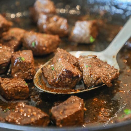 balsamic steak bites seared and cooked in cast iron skillet with metal spoon lifting them out