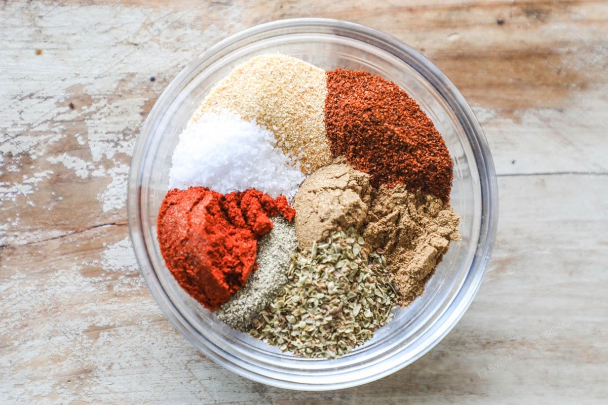 The various spices for Carne Asada Seasoning Blend in a clear bowl on a wooden background