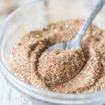 Carne Asada Seasoning Blend mix together in a clear bowl with a spoon coming out. On a wooden background