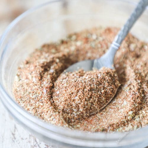Carne Asada Seasoning Blend mix together in a clear bowl with a spoon coming out. On a wooden background