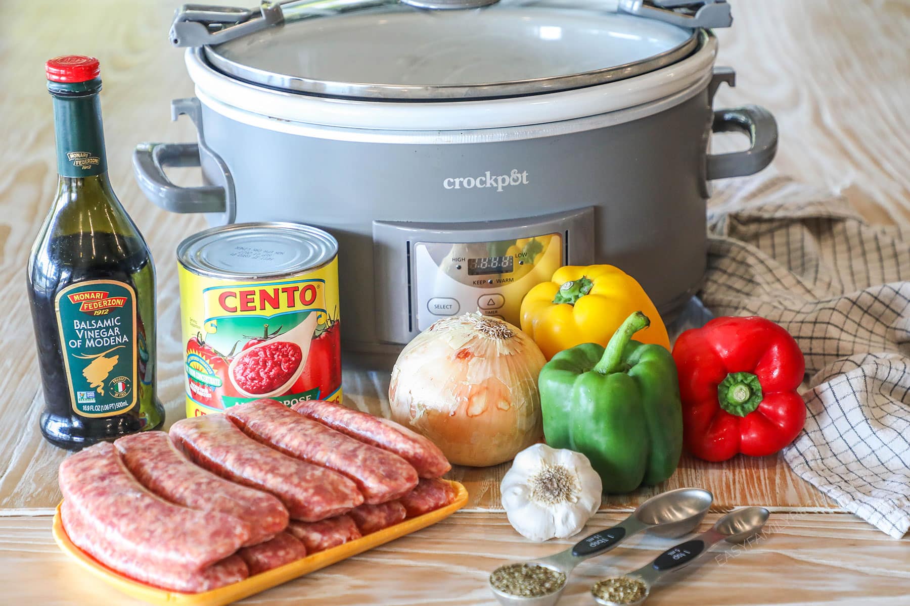 Ingredients needed to make crockpot sausage and peppers on a wooden background.