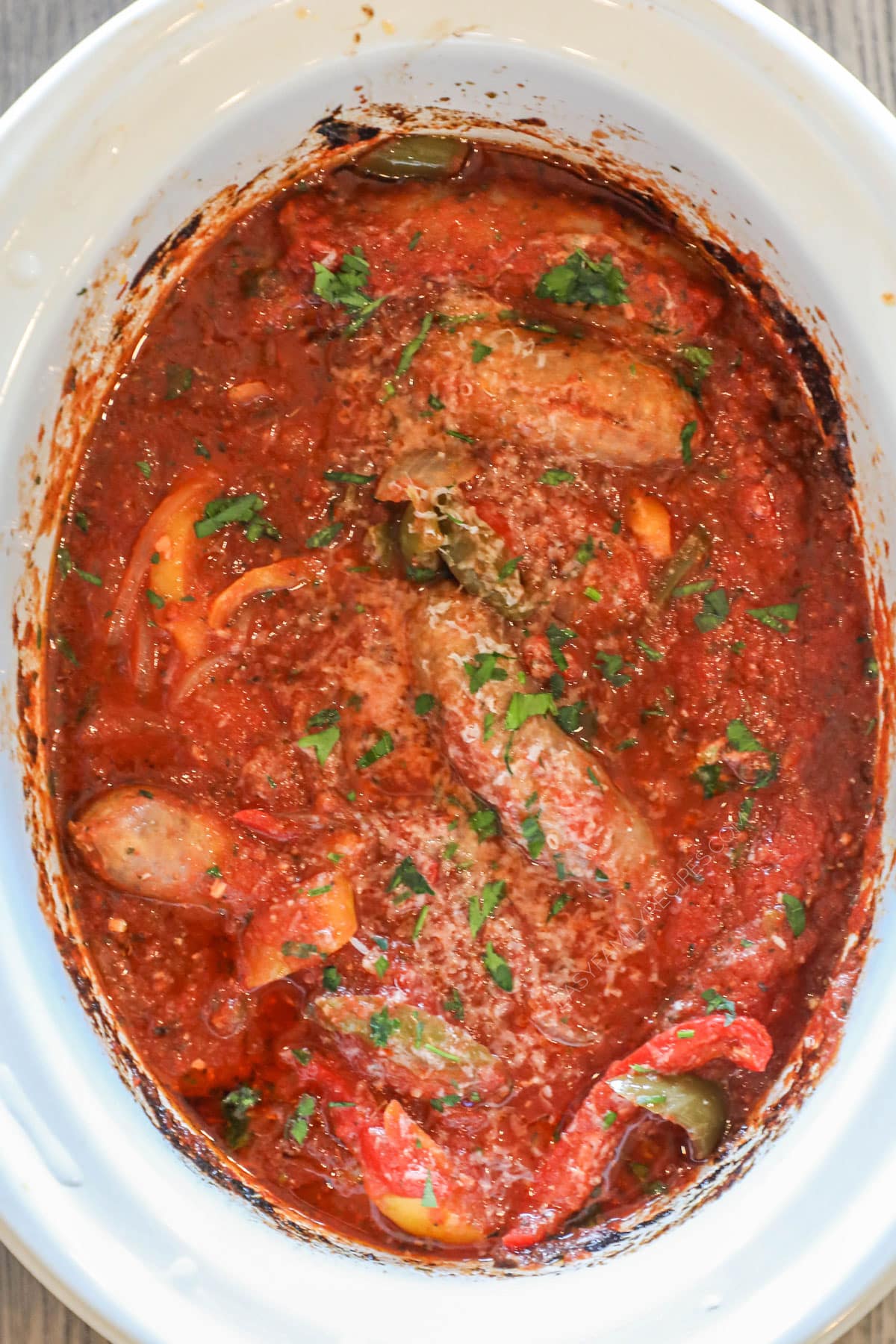 Finished crockpot sausage and peppers in the slow cooker, sprinkled with parsley.