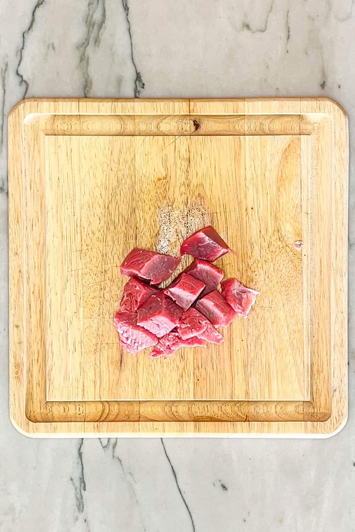step one for making steak bites on a wooden cutting board