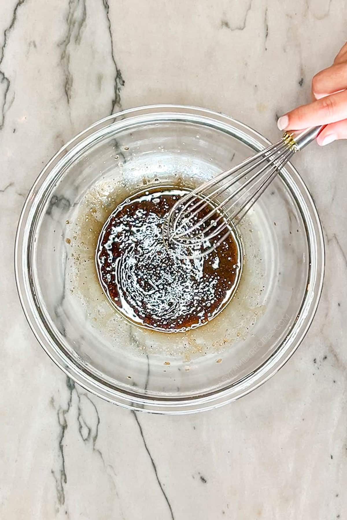 clear bowl of marinate being whisked- on a marble counter