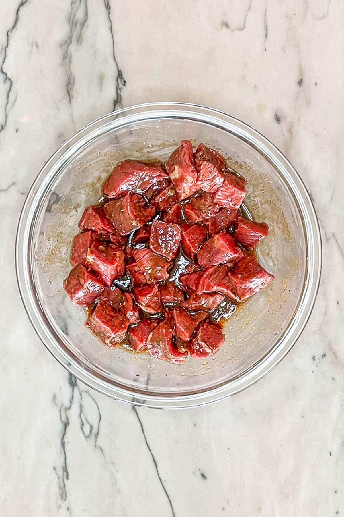 steak bites in marinade in glass bowl- on marble counter