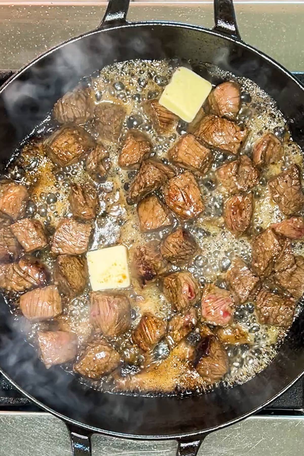 steak bites searing in a pan with two pats of butter
